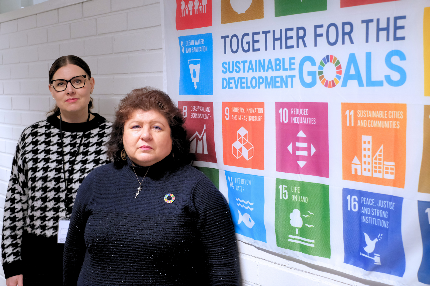 kaksi naisopettajaa seisoo YK:n vastuullisuusohjelma lipun edessä